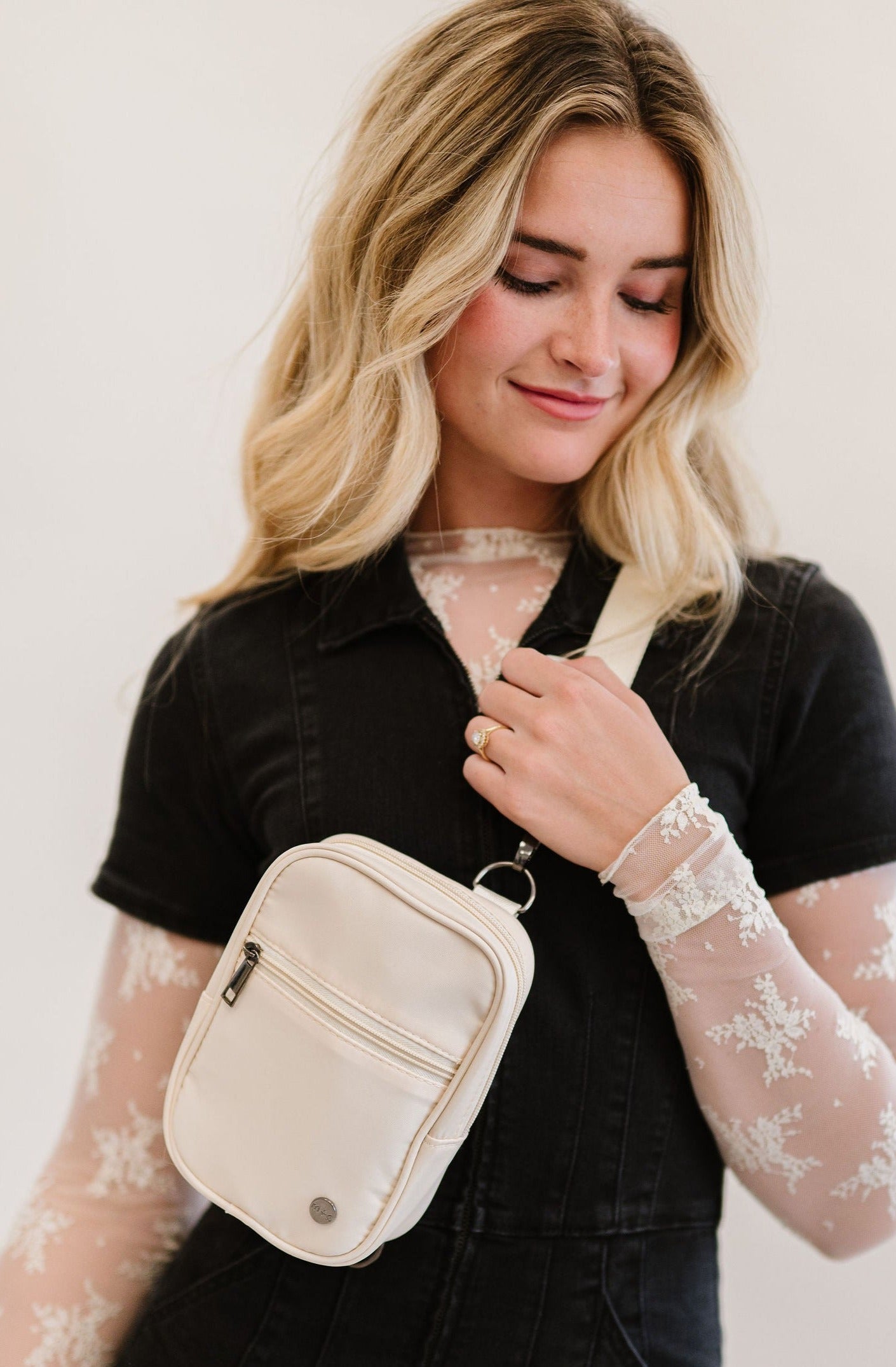 A woman wearing a lace long sleeve top under a black jumpsuit and a white Drury Road Lainey Convertible Crossbody Bag for Women crossbody.