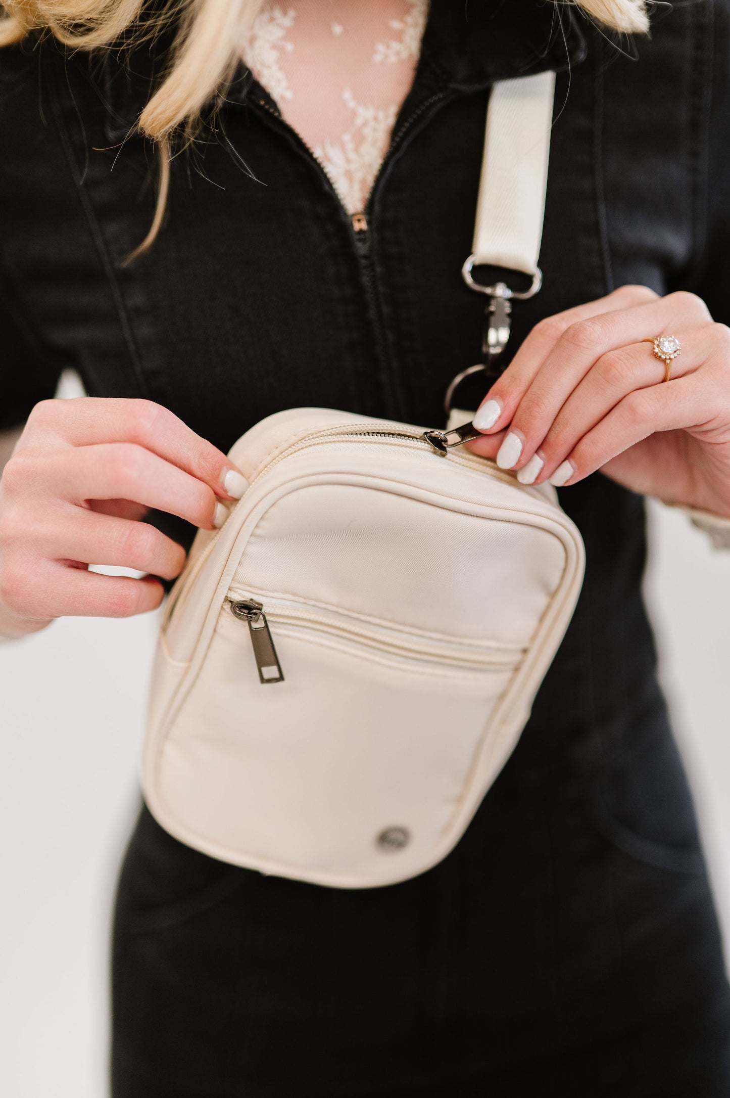 A closeup shot of a woman wearing a lace long sleeve top under a black jumpsuit and a white Drury Road Lainey Convertible Crossbody Bag for Women crossbody.