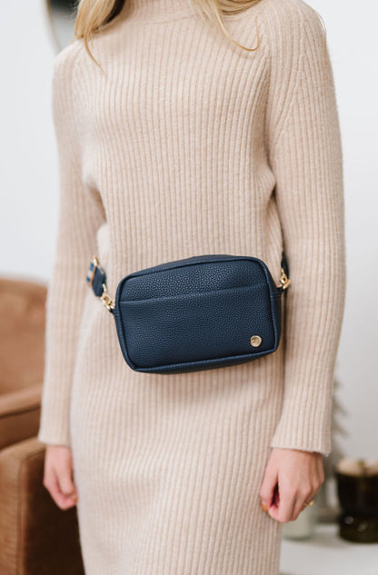 Woman wearing a blue Drury Road Willow Vegan Leather Convertible Crossbody Bag around her waist as a belt bag on a white background. 